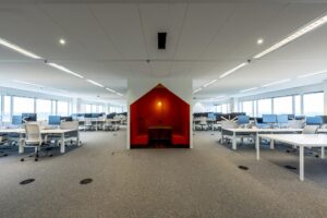 Modern open kantoorinterieur aan de Johan Huizingalaan met werkplekken en een rode afgescheiden zitruimte.